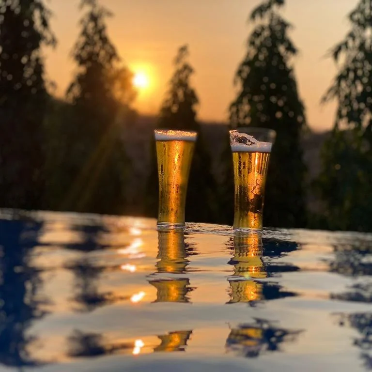 Dois copos de cerveja gelada com pôr do sol ao fundo